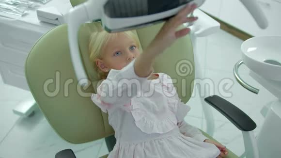 小女孩坐在牙医椅上触摸一盏灯视频的预览图