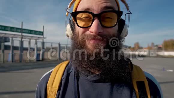 一个穿着黄色衣服戴耳机欣赏音乐的时髦留胡子男人的肖像蓝蓝的天空背景视频的预览图