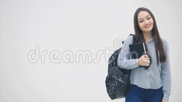 一个亚洲女学生站在她的肩膀上拿着书靠近胸部竖起大拇指视频的预览图