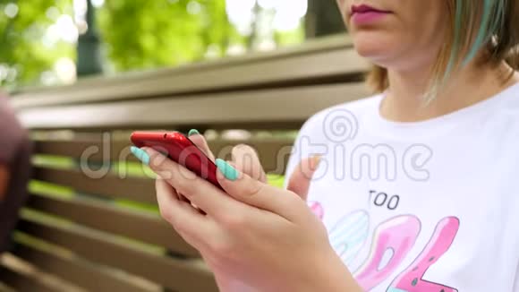 女人用智能手机坐在夏季公园的长椅上视频的预览图