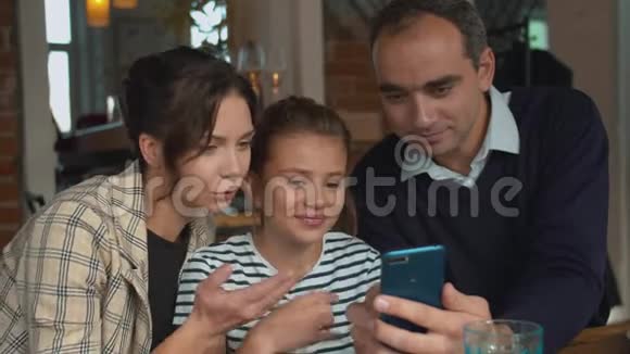 父母和女儿在午餐时通过电话观看照片视频的预览图