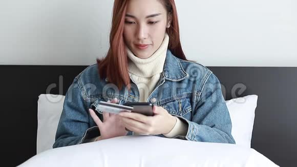 美丽的女人穿着牛仔裤夹克用智能手机上网购物用信用卡在家里生活视频的预览图