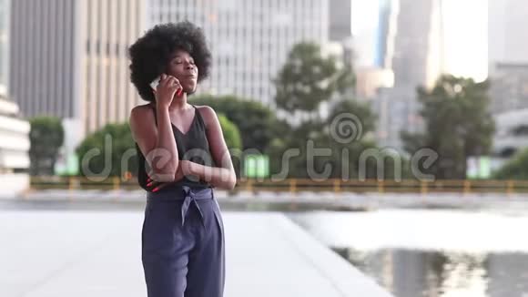 年轻的非洲妇女在喷泉边与城市背景的摩天大楼通话视频的预览图