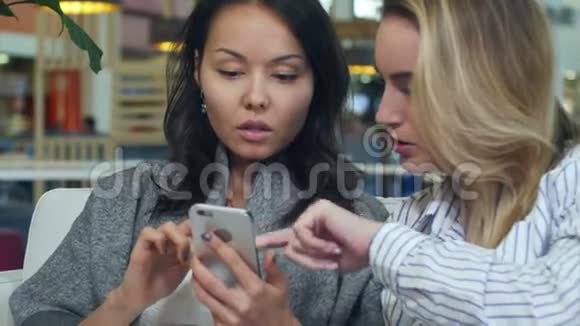 快乐购物亚洲女人与金发朋友在购物中心使用智能手机视频的预览图
