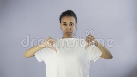 穿着白色T恤的漂亮少女拇指朝下双手放在灰色背景上视频的预览图