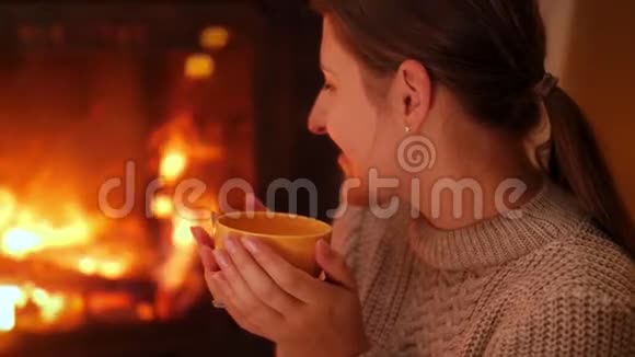 微笑的年轻女子在火宫里看着火晚上喝热茶的画像视频的预览图