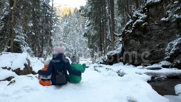 妈妈带着两个儿子在白雪覆盖的森林背景下拥抱冬季阴天背面视频的预览图