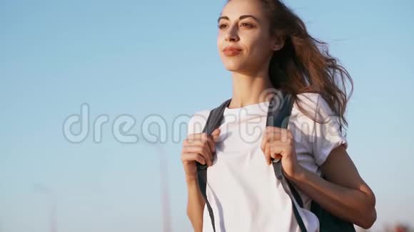 穿着白色t恤和红色裙子的年轻漂亮女人正站在蓝天的背景上看着视频的预览图