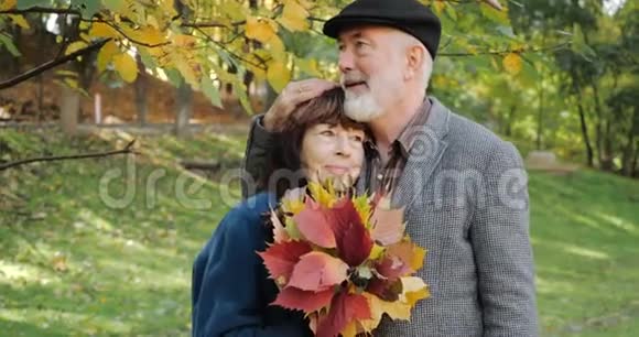 幸福的夫妻拥抱在树枝下享受秋天在树间舒适的公园里慢动作视频的预览图
