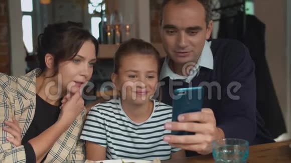 父母和女儿在咖啡馆打电话看照片视频的预览图