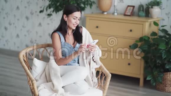 美丽的黑发女人坐在椅子上有格子呢使用智能手机视频的预览图