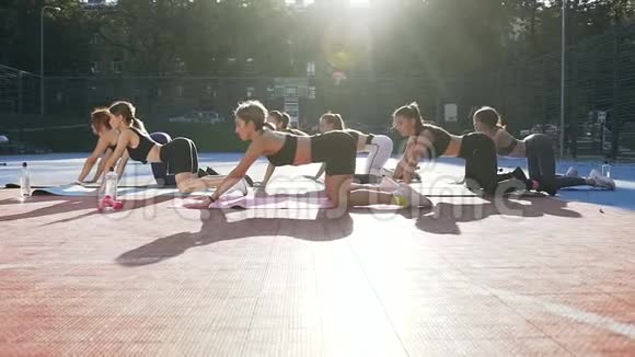 七个穿运动服装的漂亮女孩躺在垫子上在公园运动场上做放松运动视频的预览图