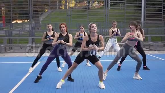 女子健身队在运动场上用哑铃运动的女性健身队的正面景色环绕着绿树视频的预览图