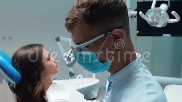 年轻的牙医戴着医用手套戴着口罩检查年轻的黑发女子病人使用牙科器械的牙齿视频的预览图
