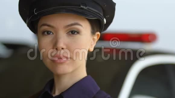 戴着帽子的亚洲女警察看着镜头微笑着站在警车旁视频的预览图