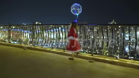 快乐的孩子在夜晚的城市散步圣诞节的光照穿着圣诞礼服的小女孩走着视频的预览图