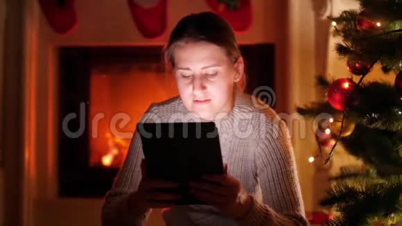 美丽的微笑的女人在家里圣诞树旁边的火炉边喝茶一边取暖视频的预览图