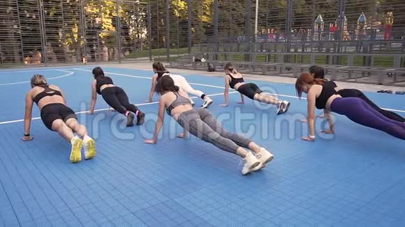 漂亮的年轻苗条的女士穿着运动服在公园的运动场上做木板视频的预览图