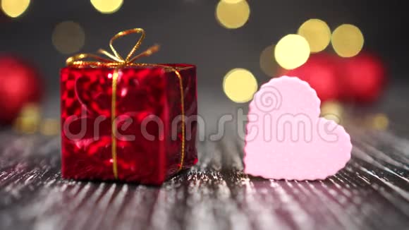 红色礼盒搭配金结和粉心特写背景中鲜艳的装饰球圣诞树灯闪烁视频的预览图