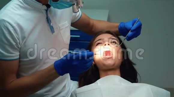 戴手套的牙医在牙科诊所预约时使用牙科镜牙坝治疗病人的牙齿视频的预览图