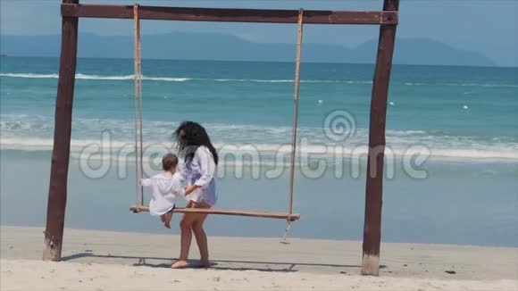 年轻的黑发女孩和她的儿子在海滩上荡秋千暑假玩得开心视频的预览图