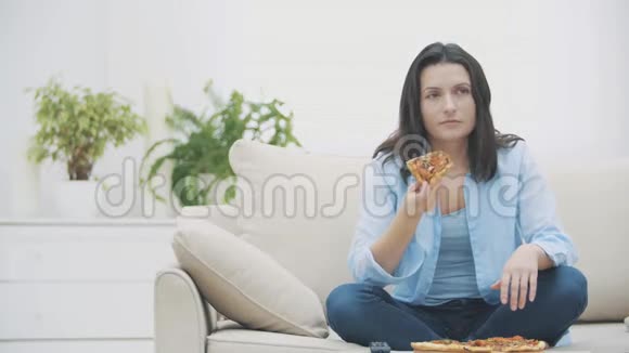饥饿的女人正在打开电视节目而坐在沙发上她在吃披萨4K视频的预览图