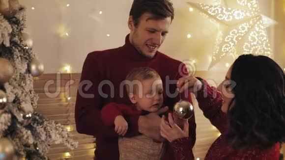 靠近年轻漂亮的母亲英俊的父亲和可爱的婴儿在圣诞树附近的父亲怀里微笑母亲视频的预览图