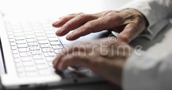 在笔记本电脑上工作的老皱纹手的特写视频的预览图