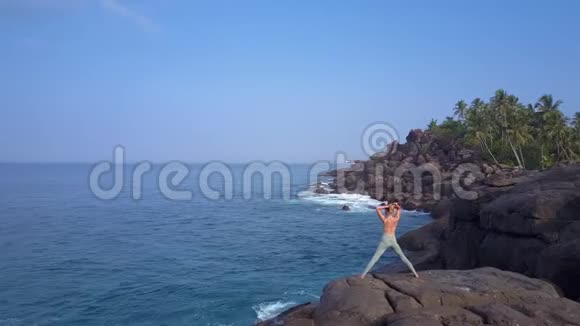 苗条的女士把发髻立在海边的大石头上视频的预览图