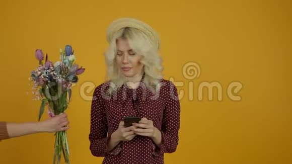 戴着帽子的漂亮金发女孩在智能手机上打字拒绝郁金香花束视频的预览图