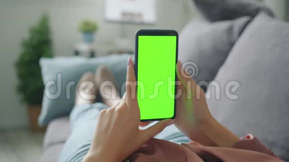 特写双手握着绿色屏幕智能手机在家中沙发上放松视频的预览图