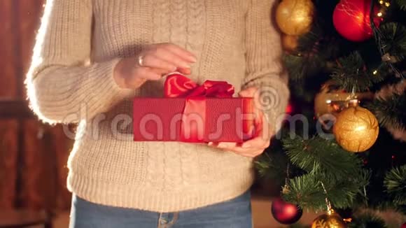 4k视频穿毛衣的年轻女子站在圣诞树旁边打开带有礼物的红色盒子视频的预览图