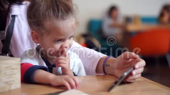 一个小可爱的欧洲人模样的女孩正坐在妈妈的手上桌子上看着她身体上的视频视频的预览图
