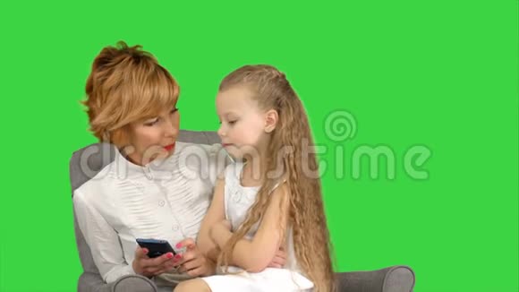 年轻的母亲和孩子在绿色屏幕上看电话Chroma键视频的预览图