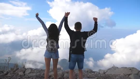 年轻的一对游客背着背包登上山顶举起双手站在边缘的男人和女人视频的预览图