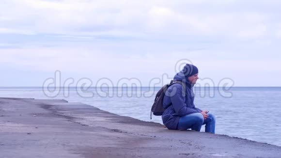 男子游客坐在老海滨冬天用电话看海视频的预览图