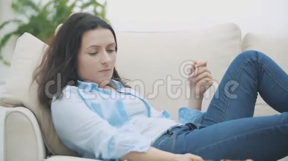 漂亮的女人躺在家里的沙发上一边吃披萨一边看电视4K视频的预览图