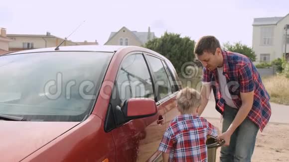 一个金发的小男孩我在他年轻父亲的监护下洗车前灯慢动作视频的预览图