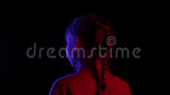 微笑的女孩转身看着相机在黑暗的工作室与红色和蓝色的照明美丽的女孩摆在面前视频的预览图