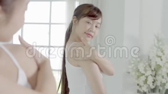 美丽的年轻亚洲女人照镜子用肩膀涂防晒霜视频的预览图