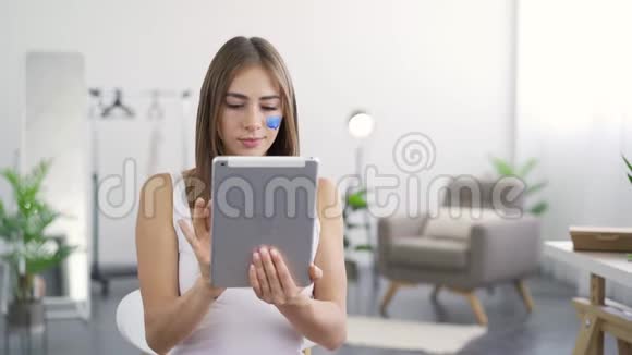 年轻迷人的女人的肖像脸上画着蓝色的社交媒体图标看着她的平板电脑微笑着视频的预览图