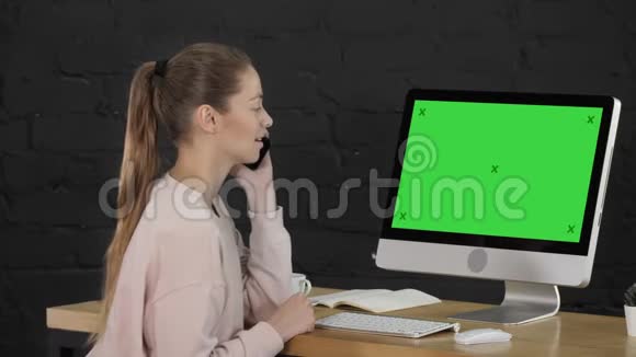可爱的女性穿着粉红色便服在电脑显示器前打电话绿屏模拟显示视频的预览图