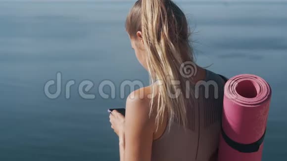 从背面看运动员女孩手里拿着手机背景是海洋视频的预览图