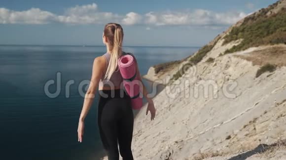 从侧面看身穿运动服的女人站在悬崖边上张开双臂视频的预览图
