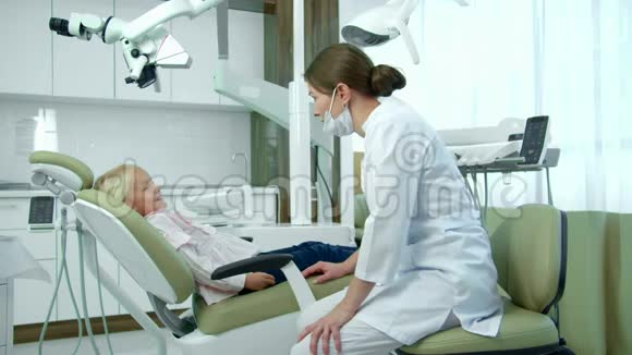戴口罩的女牙医在诊所里和一个小女孩说话视频的预览图