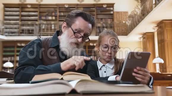 漂亮的老胡子爷爷和他漂亮的孙女坐在图书馆的桌子旁比较着印刷品视频的预览图