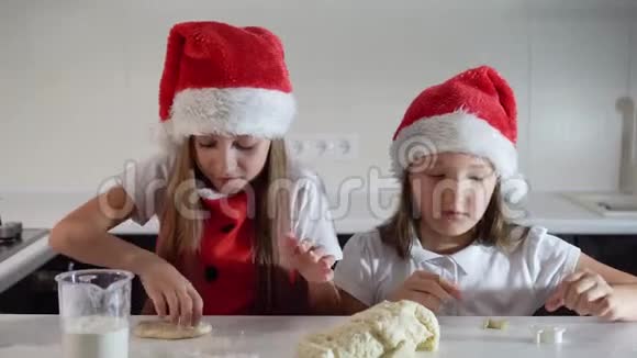 两个可爱的小女孩戴着圣诞老人的帽子围着红色的圣诞围裙亲手做饼干微笑新年快乐视频的预览图
