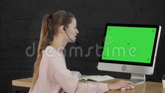 微笑的年轻女性戴着耳机在监视器前打电话绿屏模拟显示视频的预览图