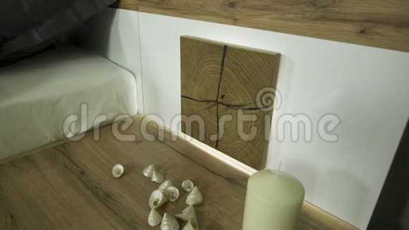 木制床头柜上有一支蜡烛和散落的装饰贝壳视频的预览图