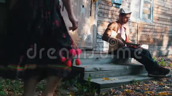 一个女人在音乐旁边跳舞在房子附近玩得很开心一个男人在演奏巴拉莱卡阳光穿过视频的预览图